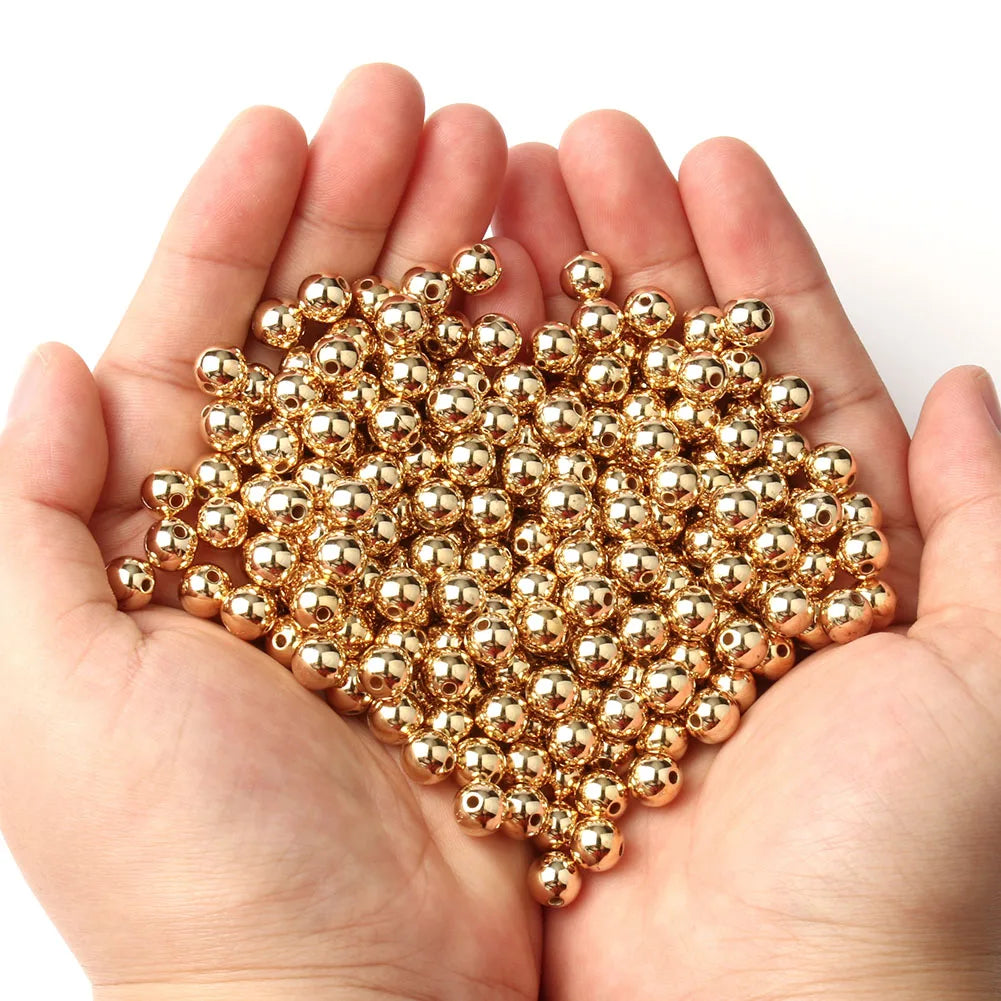 A hand holds a pile of round gold spacer beads for DIY jewelry making