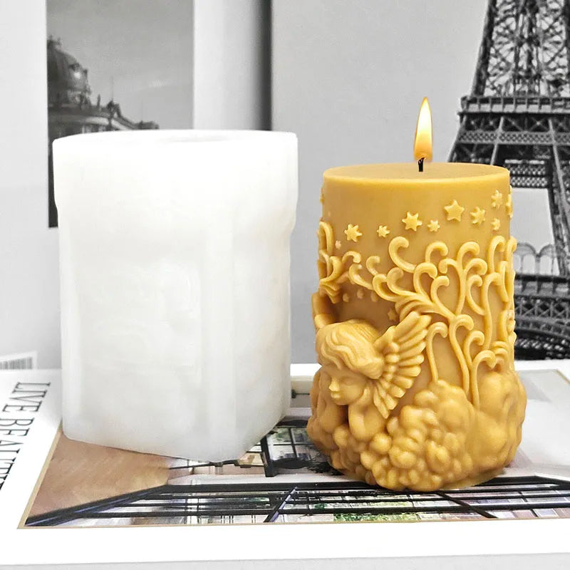 A golden silicone mold shaped like an angel is shown next to a white pillar candle and a lit candle.