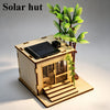 A wooden model kit of a solar hut featuring a solar panel on the roof and a small plant.