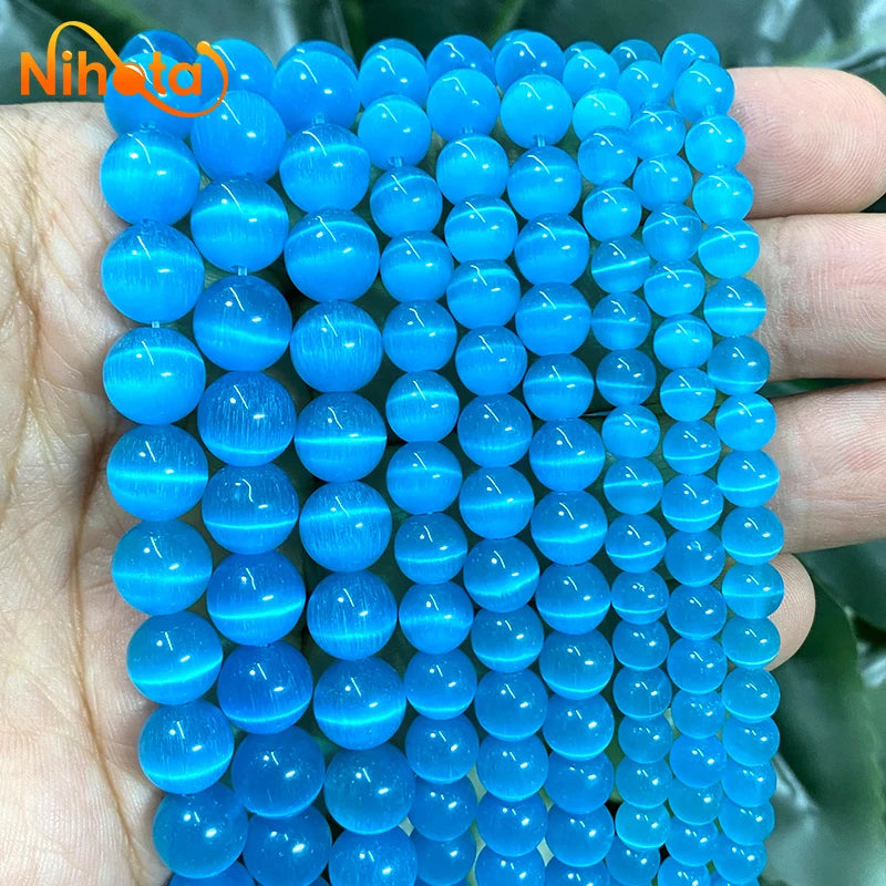 A hand holds a strand of bright blue cat eye stone beads for jewelry making