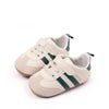 A pair of beige baby first walkers shoes with green stripes and soft suede material.