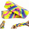 A rectangular squishy butter stick fidget toy in neon pink and yellow colors is shown alongside a flexible silicone band.
