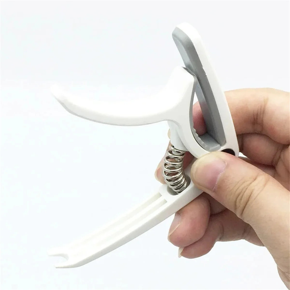 A hand holds a white universal guitar capo, showing the clamping mechanism and the capo itself.