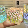 A hand holds a clear cube night light craft kit filled with pink and white tulip flowers.