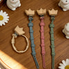 A set of three baby pacifier clips with burlap flower designs displayed on a wooden tray.