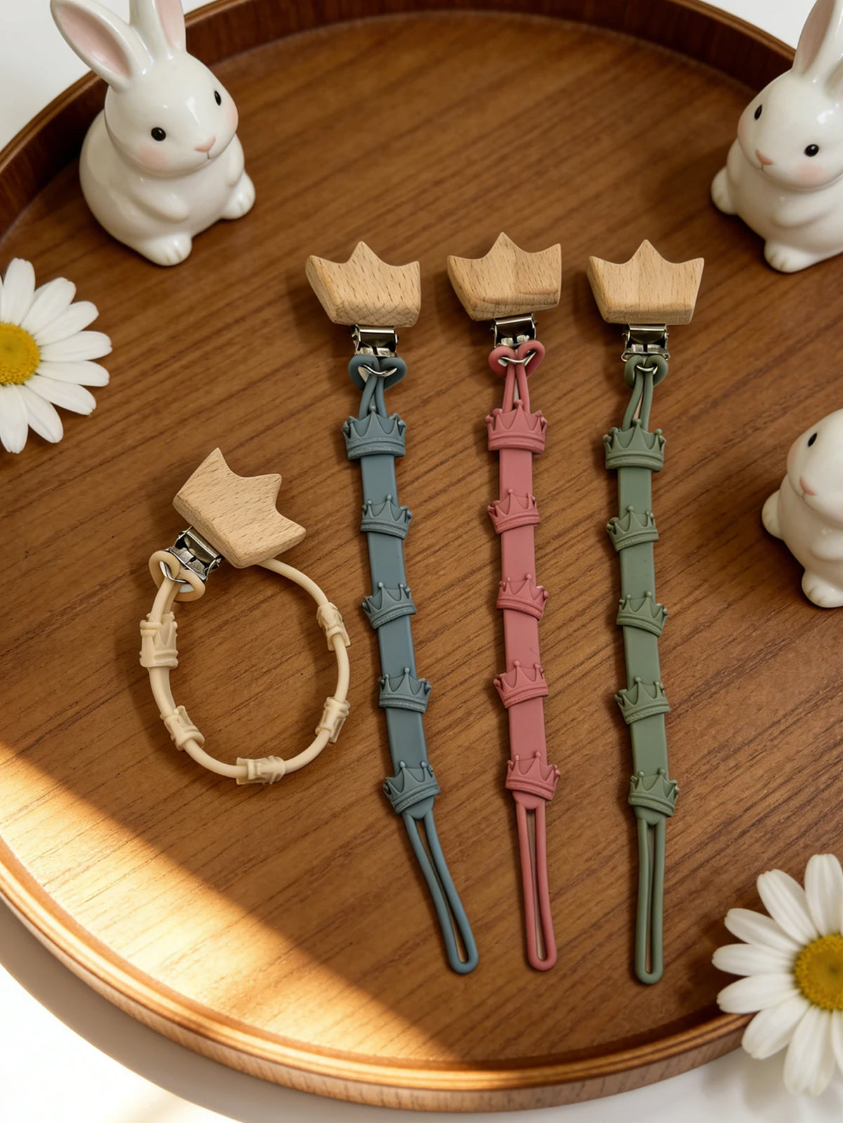 A set of three baby pacifier clips with burlap flower designs displayed on a wooden tray.