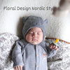 A newborn baby wearing a gray hooded outfit and holding a natural latex pacifier on a white blanket.