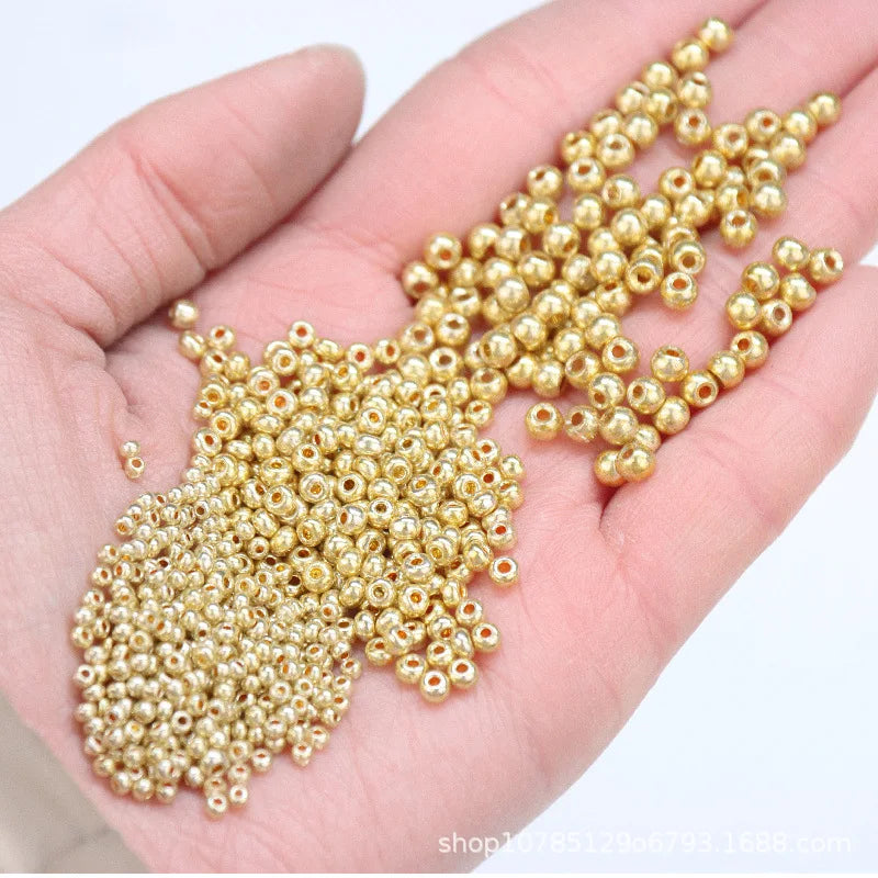 A hand holds a cluster of small, gold-colored metallic glass beads for jewelry and crafting.