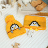 A yellow knit penguin hat and scarf set with black accents resting on a white surface.