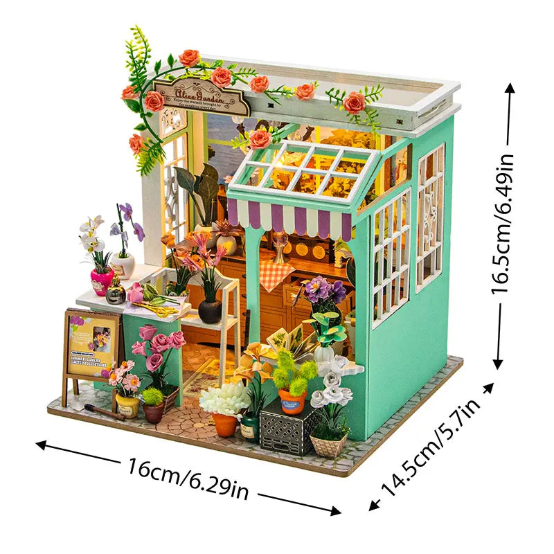 A miniature dollhouse kit featuring a green and pink wooden structure with furniture, plants, and warm lighting elements.