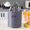 A purple stackable bento lunch bag with a handle sits on a white table next to juice bottles.