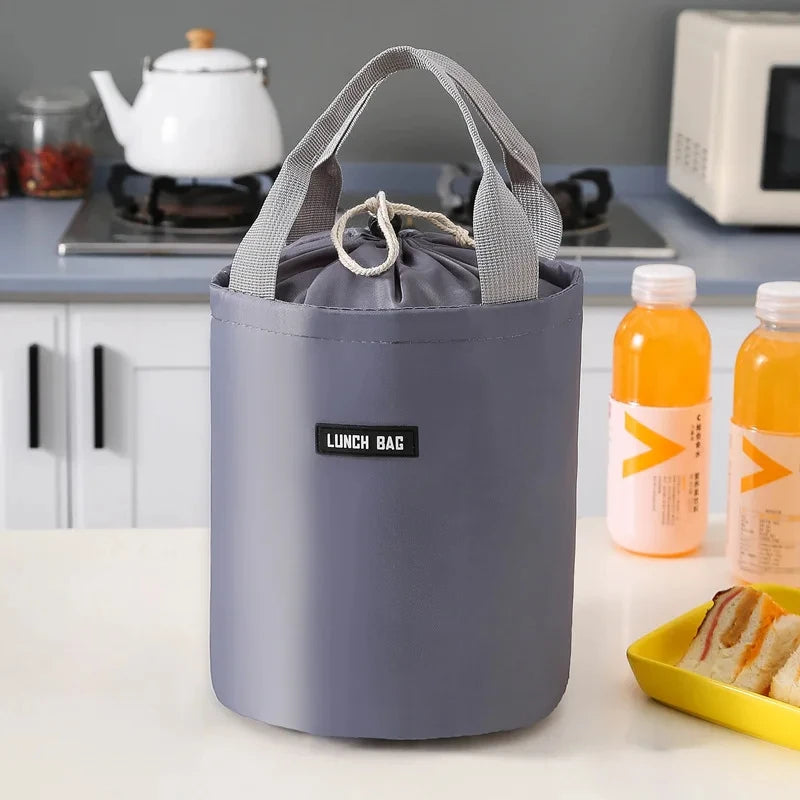 A purple stackable bento lunch bag with a handle sits on a white table next to juice bottles.