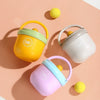 A collection of three insulated stainless steel breakfast cups in yellow, green, and purple resting on a pink textured surfac