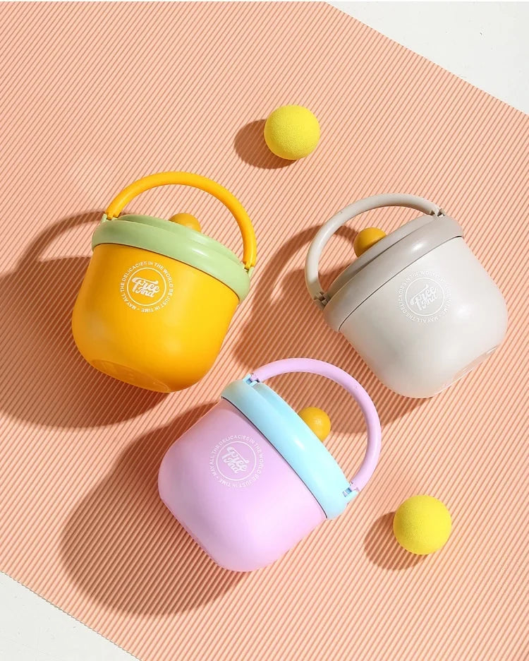 A collection of three insulated stainless steel breakfast cups in yellow, green, and purple resting on a pink textured surfac
