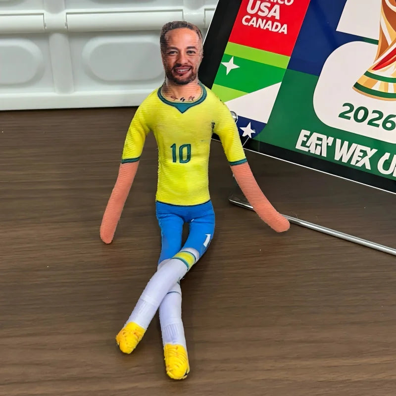 A man dressed in a yellow football jersey and blue pants stands on a wooden floor in front of a banner.