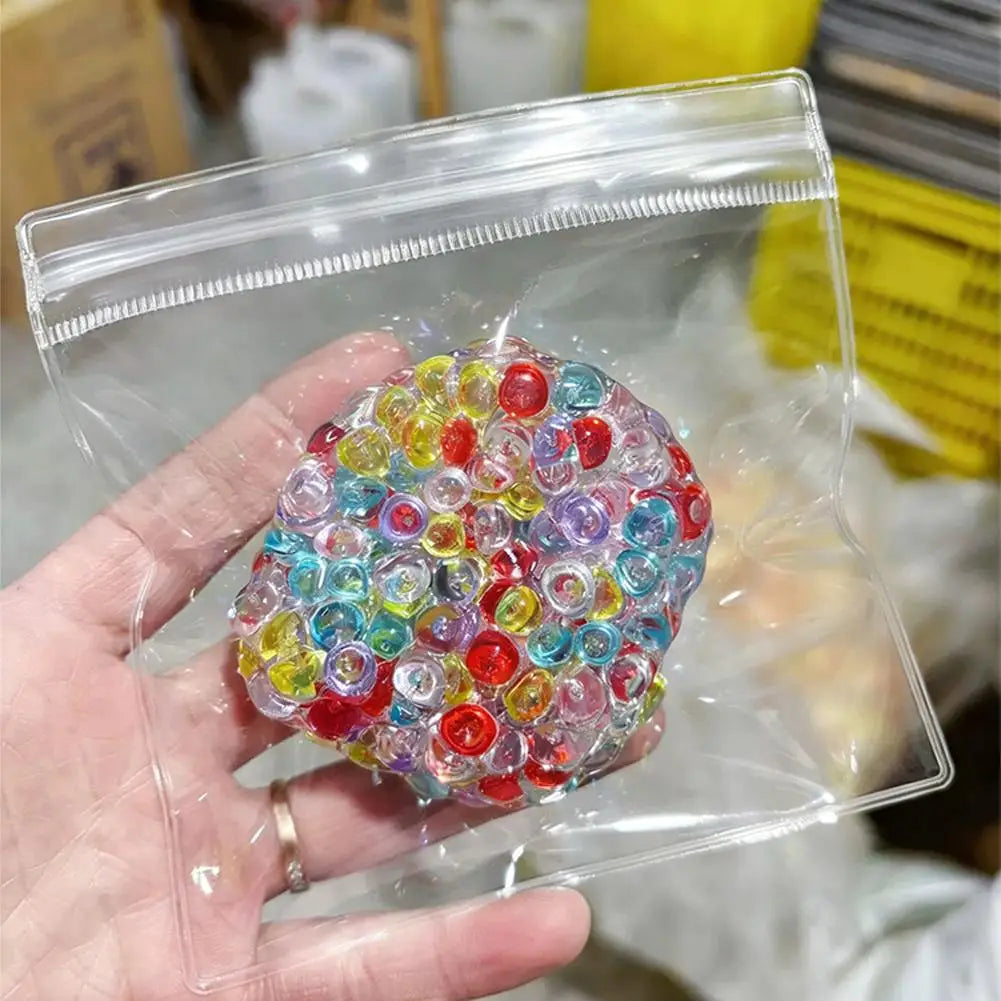 A hand holds a clear plastic bag filled with colorful squishy beads for stress relief.