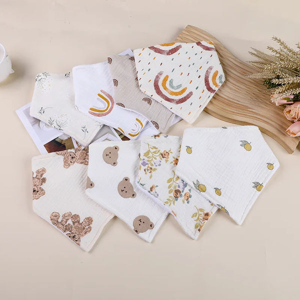 A collection of soft cotton baby bibs featuring various patterns including rainbows, leaves, and woodland animals.