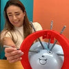 A woman is holding a red ring with several metal spikes, which is part of the Balloon Pop Party Game.