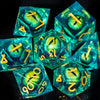 A collection of seven liquid core resin polyhedral dice in shades of teal and green resting on a dark surface.