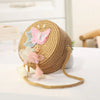 A round, handwoven straw crossbody bag decorated with pink and blue floral lace bows.