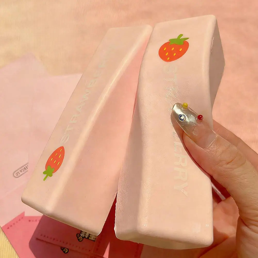 A hand holds a pink strawberry milk squishy stress relief toy with a glittery fingernail.
