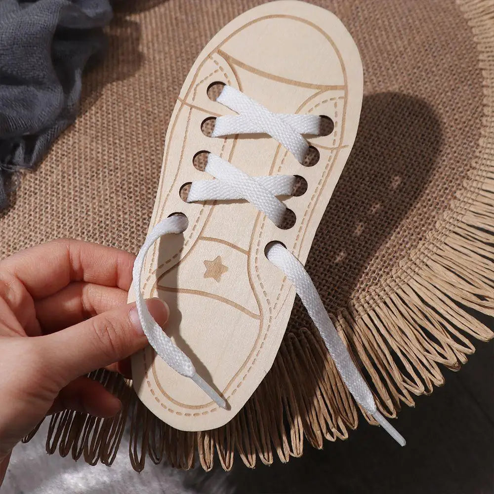 A hand holds a wooden lacing shoe toy with white laces on a woven mat.