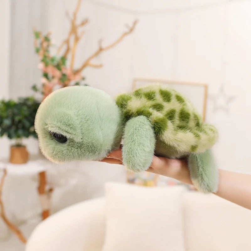 A hand holds a soft, light green Big Eyes Tortoise plush pillow with textured skin and leafy patterns.
