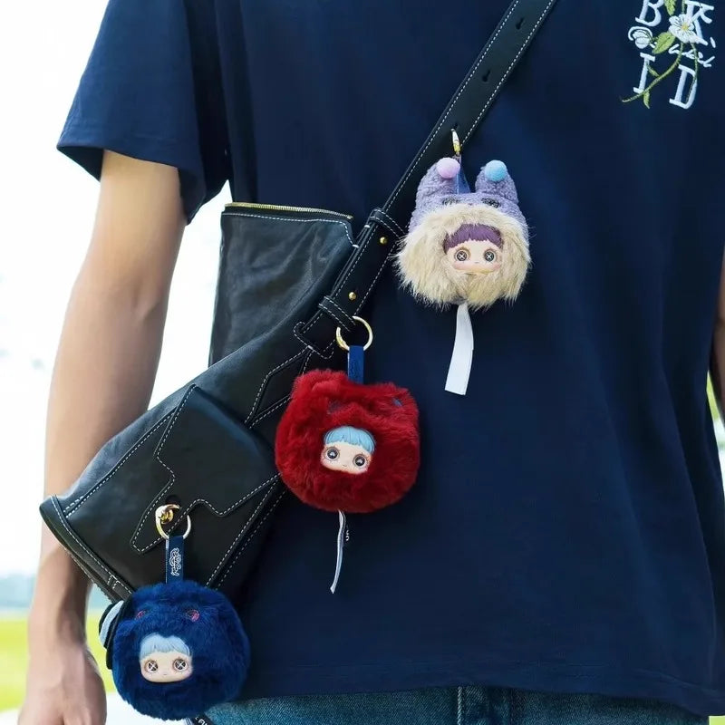 A dark blue t-shirt features a black bag clip with three plush blind boxes: a purple, a beige, and a red fluffy animal.