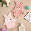 A pink fluffy plush toy shaped like a bunny is shown next to a white hot water bottle and a keyboard.