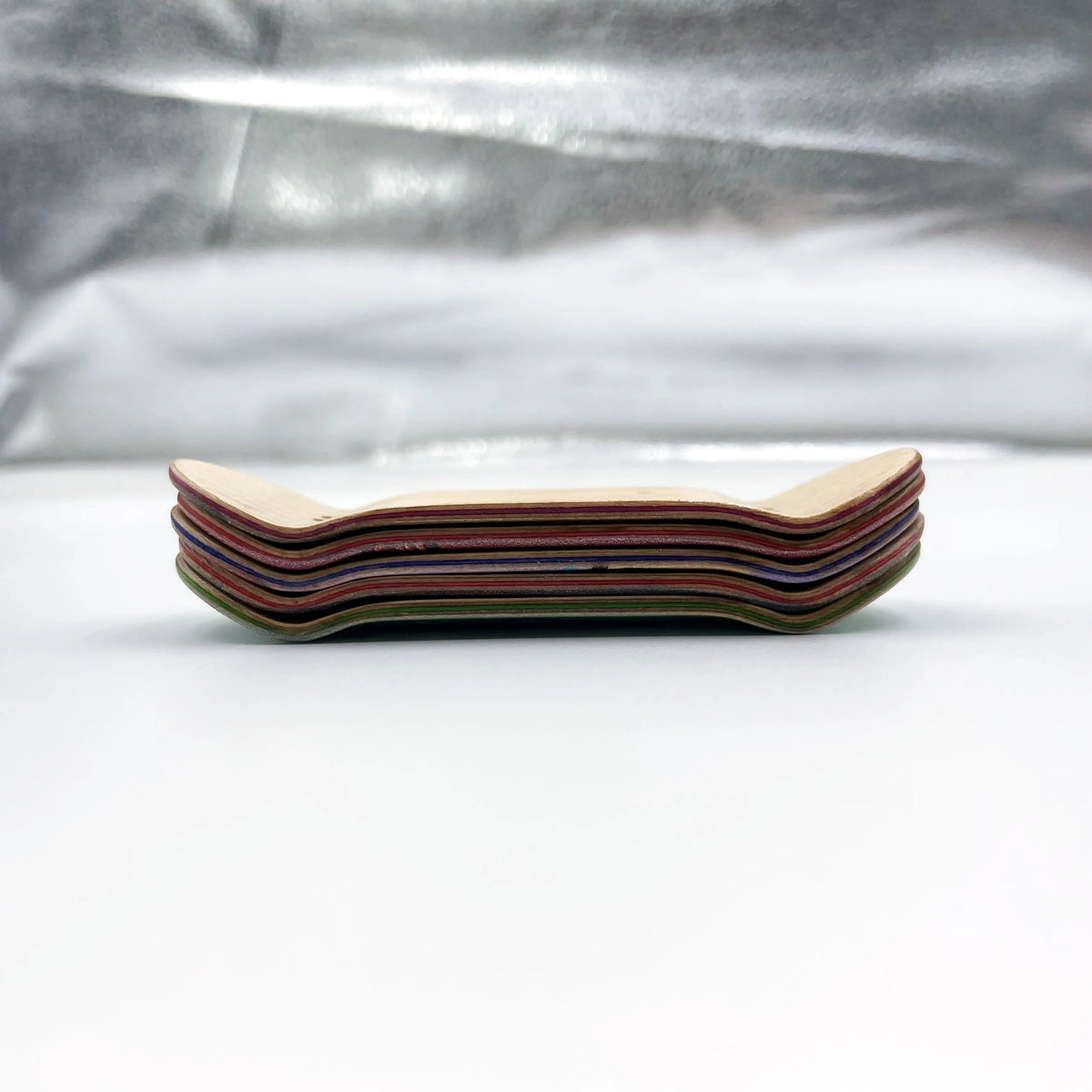 A stack of wooden fingerboard decks with UV-printed graphics arranged horizontally on a white surface.