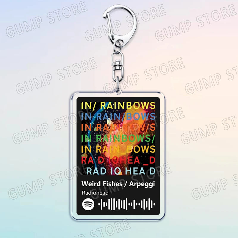 Silver acrylic keychain featuring text listing various music genres and artists like In Rainbows and Rad IQ Head D