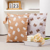 Two beige and pink reusable waterproof baby wet bags with cute animal designs are displayed on a white shelf.