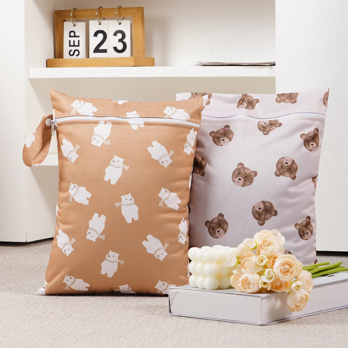 Two beige and pink reusable waterproof baby wet bags with cute animal designs are displayed on a white shelf.
