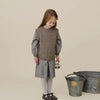 A young girl wearing a beige knit sweater and gray pleated skirt with a small basket.