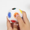 A hand is holding a white rainbow cube fidget toy with colorful, translucent spheres.