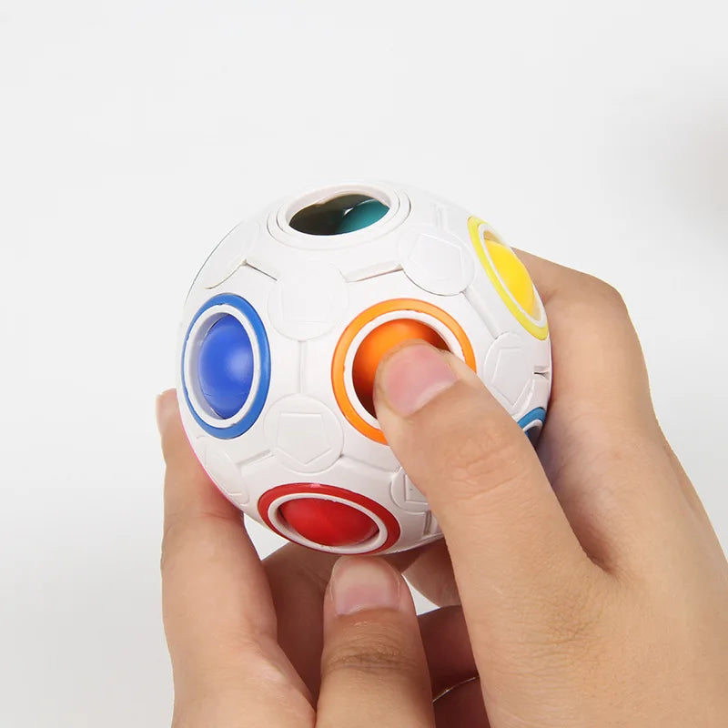 A hand is holding a white rainbow cube fidget toy with colorful, translucent spheres.