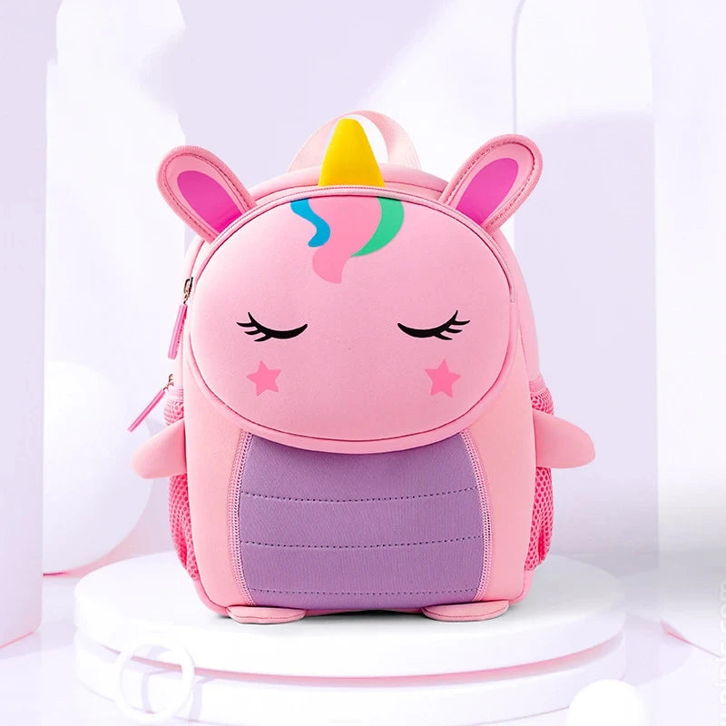 A pink unicorn backpack with closed eyes and a yellow horn resting on a white surface.