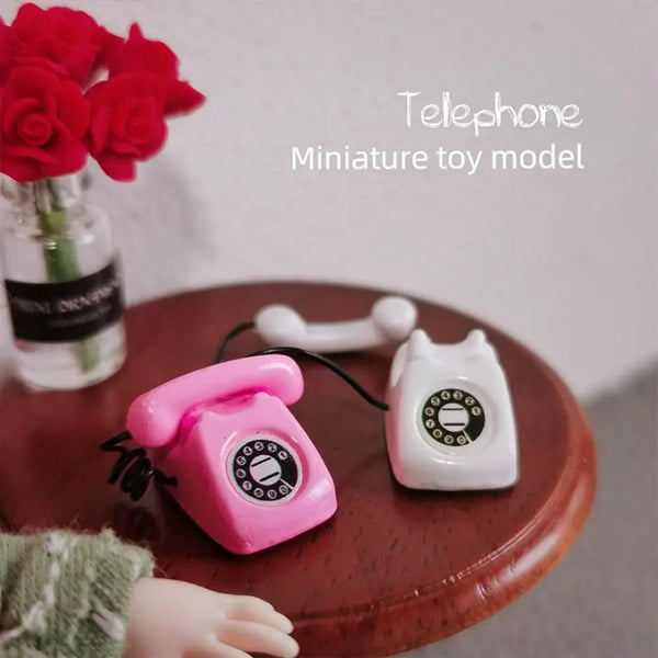 A pink miniature rotary telephone toy model resting on a wooden surface.