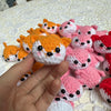 A hand holds several handcrafted crochet animal keychains in orange, pink, and red colors.