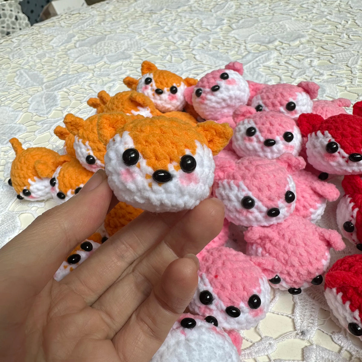 A hand holds several handcrafted crochet animal keychains in orange, pink, and red colors.