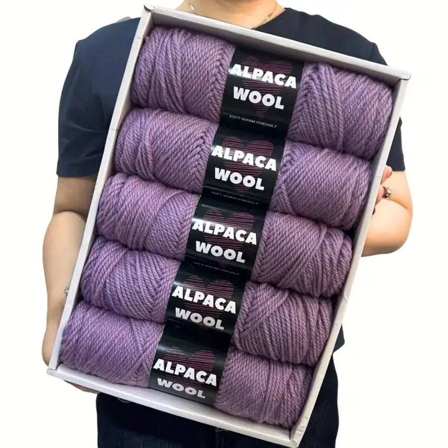 A box containing five skeins of purple alpaca wool yarn for knitting and crochet.