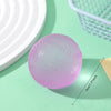A pink, textured squishy ball is shown on a light green surface next to a white plate and a green wire basket.