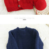 A close-up of a bright red knitted cardigan and a navy blue knitted sweater displayed on a white fluffy surface.