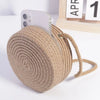 A beige handwoven straw crossbody bag with a zipper and lace bow next to an iPhone.