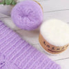 Purple silk mohair blended yarn skein next to a knitted purple sweater and a white pompom.