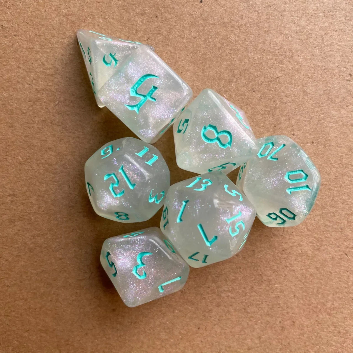 A set of seven translucent light green glitter polyhedral dice resting on a brown surface.