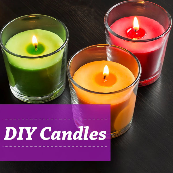 Three glass jars containing DIY candles in green, red, and orange hues with lit wicks.