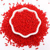 A pile of bright red polymer clay slice sprinkles scattered on a white background.