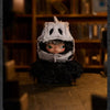 A small plush doll with a white mask and black hair is displayed on a wooden surface.
