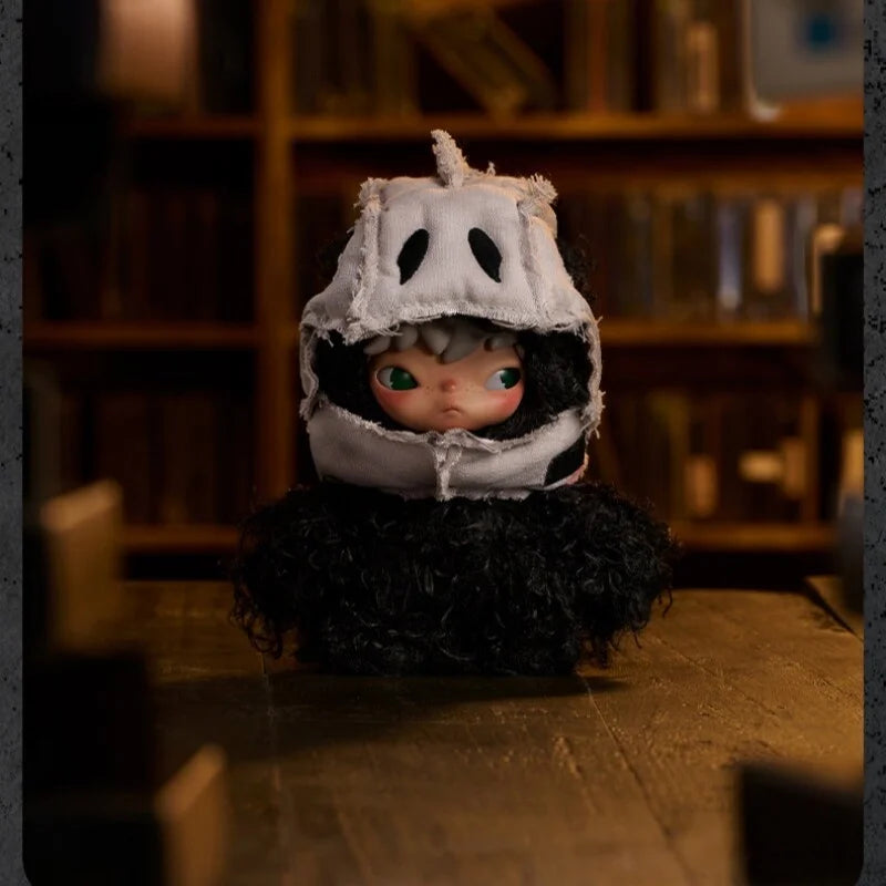 A small plush doll with a white mask and black hair is displayed on a wooden surface.